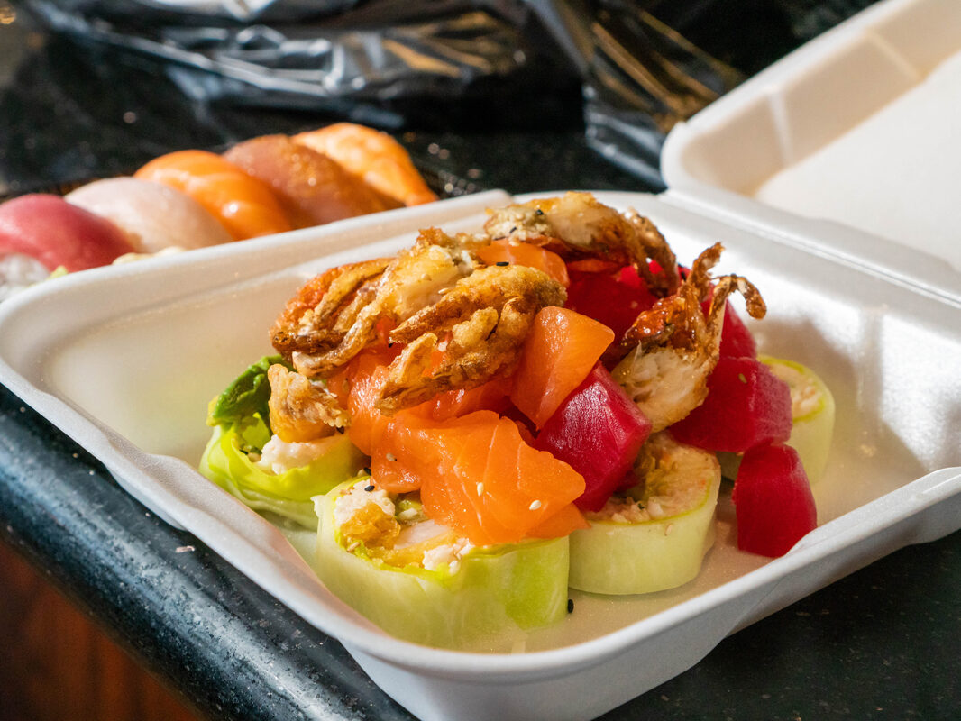 Sushi N Pop Roll in to go container with sashimi in the background